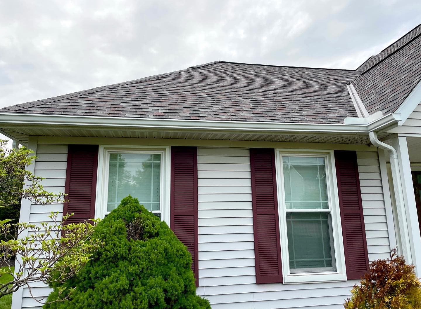 Vinyl-sided home with white seamless gutters, a corner downspout and burgundy shutters
