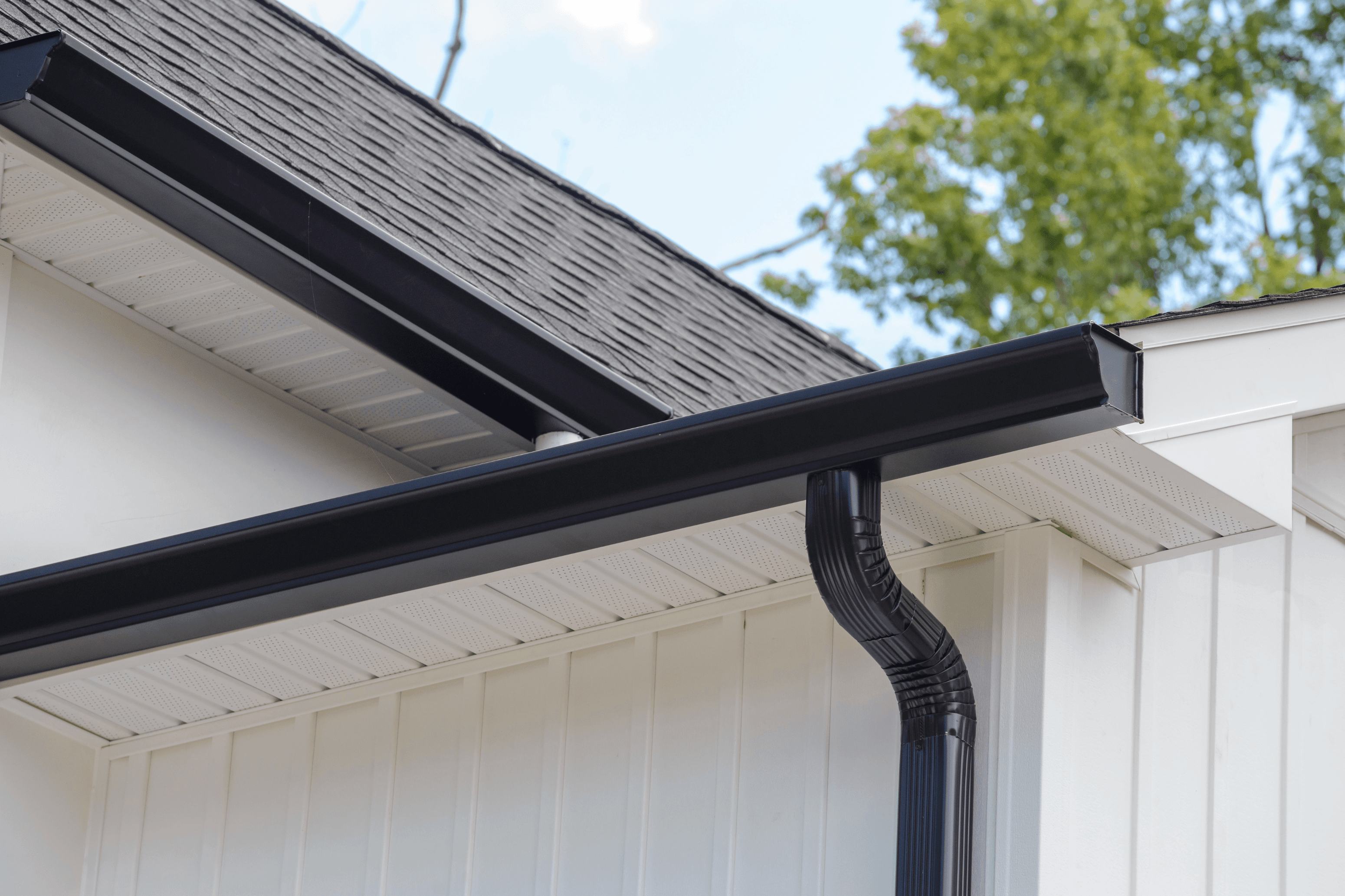 Black seamless K-style gutter and downspout on a white board-and-batten house