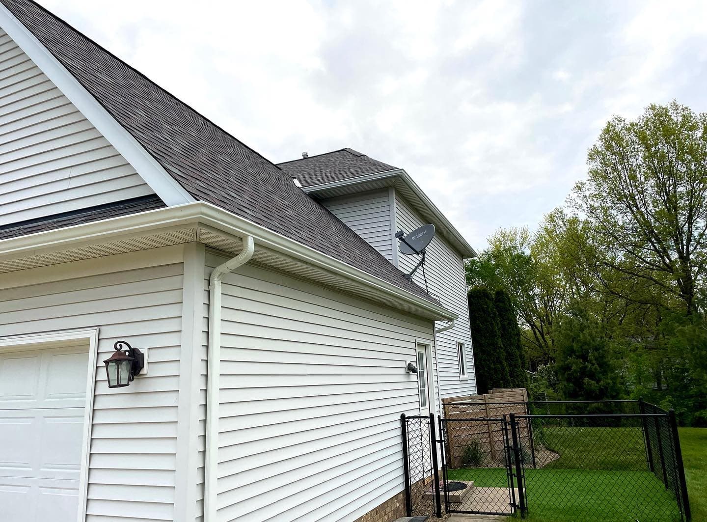 White fascia, gutter and downspout at the corner of a vinyl-sided home beside a garage