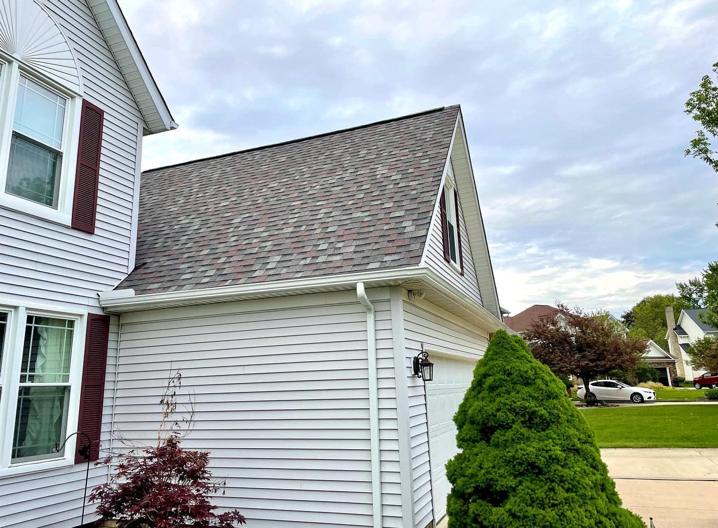 Two-story white vinyl home with burgundy shutters and white gutters beside the garage